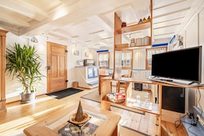 A modern living room with wooden floors, a television, a potted plant, and a dining area with a table and chairs.