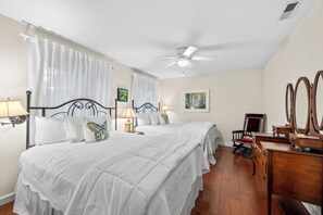A hotel room with two beds, a ceiling fan, a wooden dresser, and a chair.