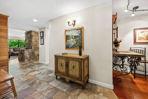 A spacious room with a stone fireplace, a dining area with a table and chairs, and a hallway with a wooden cabinet and artwork.