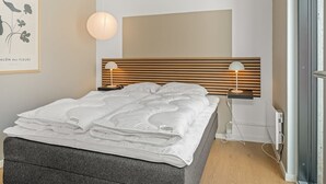 Een moderne slaapkamer met een bed, nachtlampjes, een wandlamp en een lijst met kunstwerk.