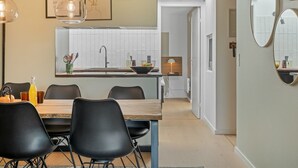 Een moderne keuken met een eetgedeelte, met een houten tafel, zwarte stoelen en hanglampen.