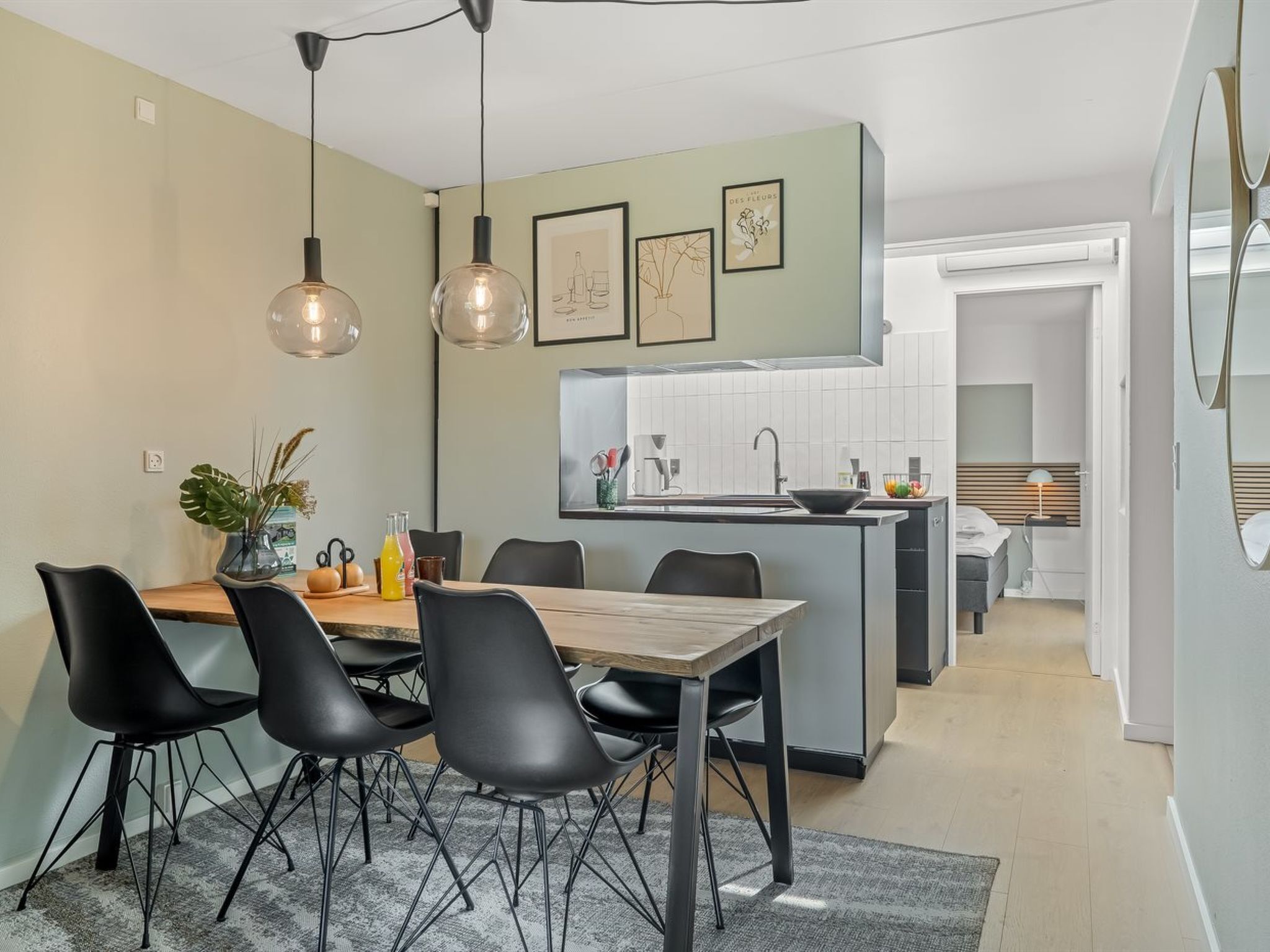 Une cuisine moderne avec un îlot central, des chaises noires et des luminaires suspendus.
