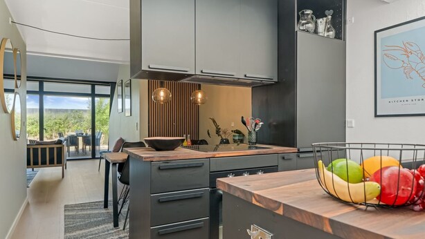 Een moderne keuken met donkere kastjes, een houten aanrecht en een schaal met fruit.