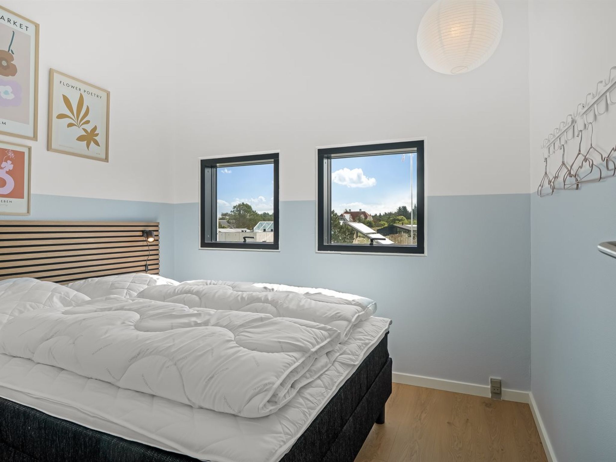 Ein Schlafzimmer mit einem Bett, zwei Fenstern, einer Wandleuchte und gerahmten Bildern.