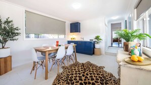 A modern kitchen with blue cabinets, a dining area with a wooden table and white chairs, and a leopard print rug. - The Palmer Cove - Stylish, Central (Dubbo)