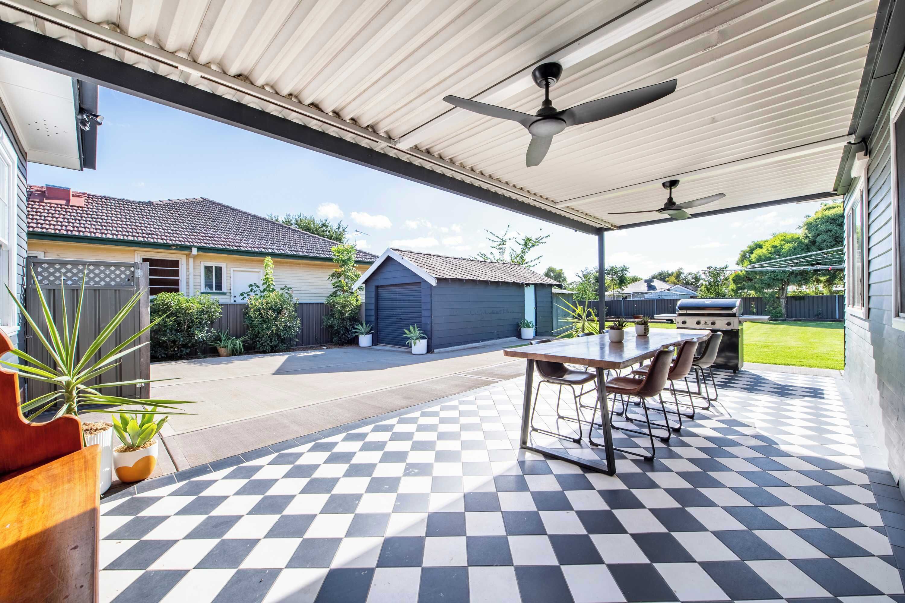 A covered patio with a checkered floor, a table with chairs, and a barbecue grill.