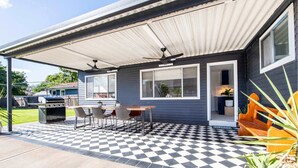 A covered patio with a checkered floor, a grill, and a table with chairs. - The Palmer Cove - Stylish, Central (Dubbo)