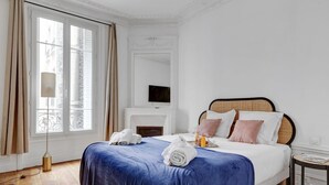 A hotel room with a large bed, a fireplace, a television, and a view of the city through the window. - TheBlueStay 318 - Apartment near the Eiffel Tower (Paris)