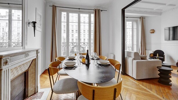 A dining area with a round table set for four, flanked by large windows with curtains, a fireplace, and a living area with a sofa and a TV. - TheBlueStay 318 - Apartment near the Eiffel Tower (Paris)