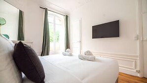 A hotel room with a large bed, a flat-screen TV mounted on the wall, and a window with curtains.