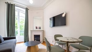 A modern living room with a sofa, a round coffee table, and a fireplace. There is a TV mounted on the wall and a dining table with chairs.