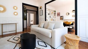 Ein modernes Wohnzimmer mit einem weißen Sofa, einem schwarzen Hocker und einem gewebten Beistelltisch.