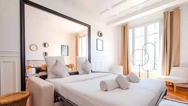 Ein Hotelzimmer mit einem großen Bett, einer Sitzecke mit einem Sessel, einem Esstisch und einem großen Spiegel.