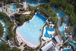An aerial view of a resort with multiple swimming pools, a large central pool, and a water slide.