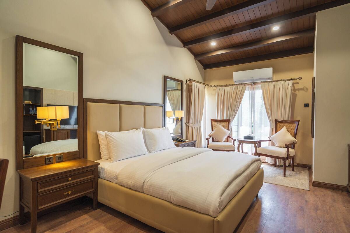 A hotel room with a large bed, a nightstand, a chair, a desk, and a mirror.