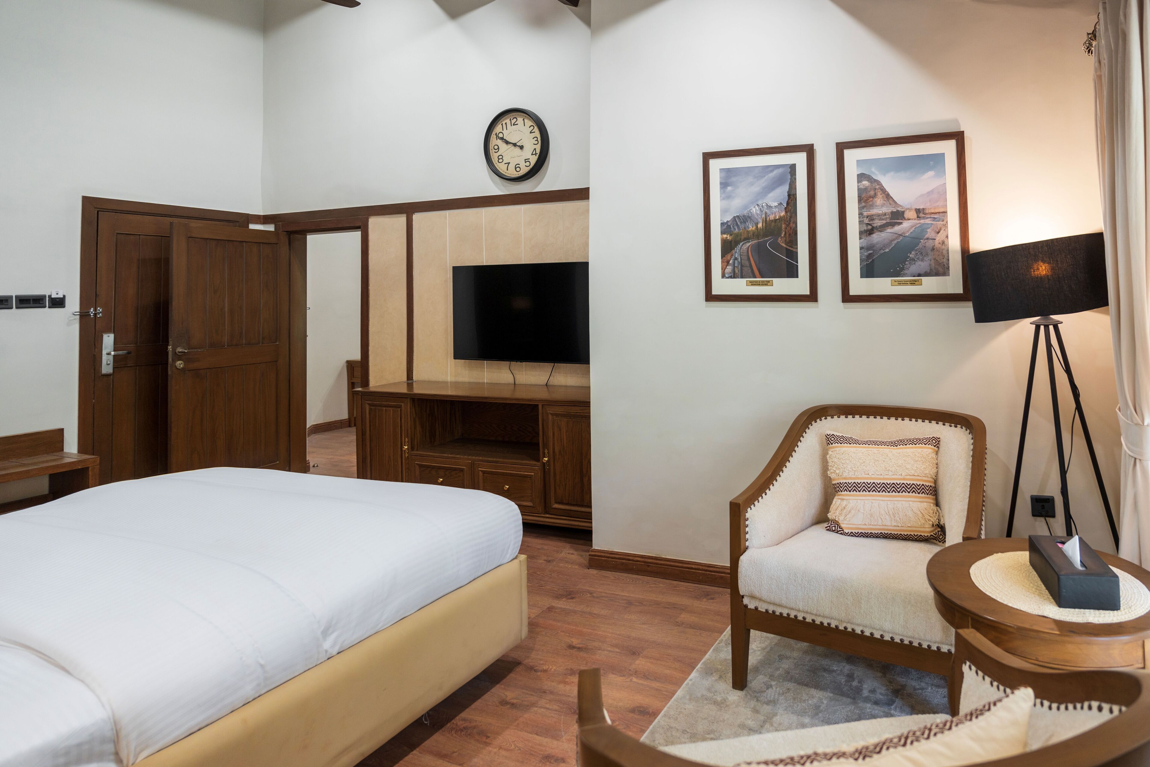 A hotel room with a bed, a chair, a TV, and two framed pictures on the wall.