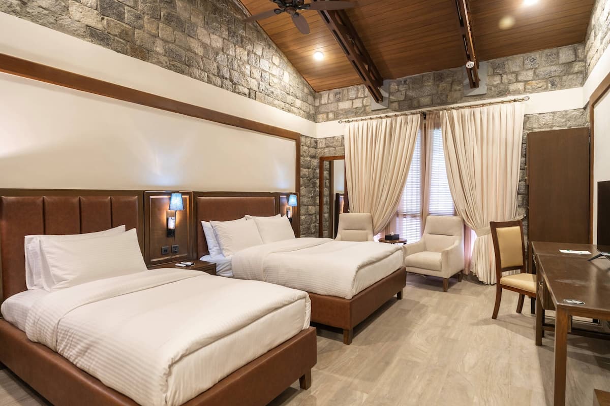 A hotel room with two beds, a desk, a chair, and a TV.