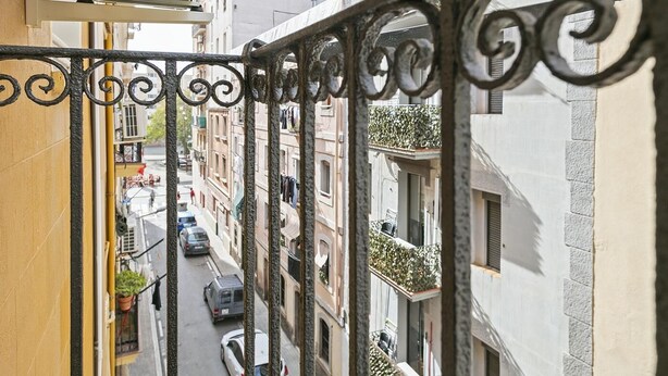 A narrow street with buildings on either side, a balcony with a metal railing, and a parked car. - Winahost La Barceloneta (Barcelona)