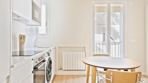A compact kitchen with a washing machine, a dining table with chairs, and a large window with a view. - Winahost La Barceloneta (Barcelona)