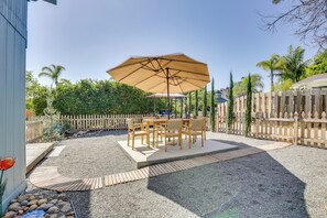 An outdoor patio with a table and chairs, a large umbrella, and a wooden fence. - Sip, Shop & Explore: San Diego Apartment (San Diego)