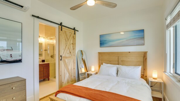 A bedroom with a bed, a nightstand, a wall-mounted painting, a ceiling fan, and a sliding barn door. - Sip, Shop & Explore: San Diego Apartment (San Diego)