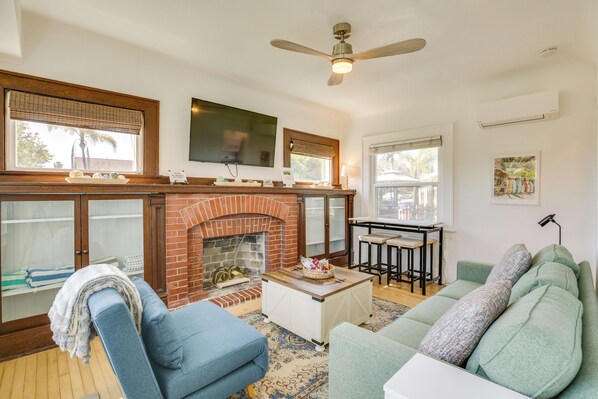 A living room with a fireplace, a ceiling fan, a television, and a dining area. - Sip, Shop & Explore: San Diego Apartment (San Diego)