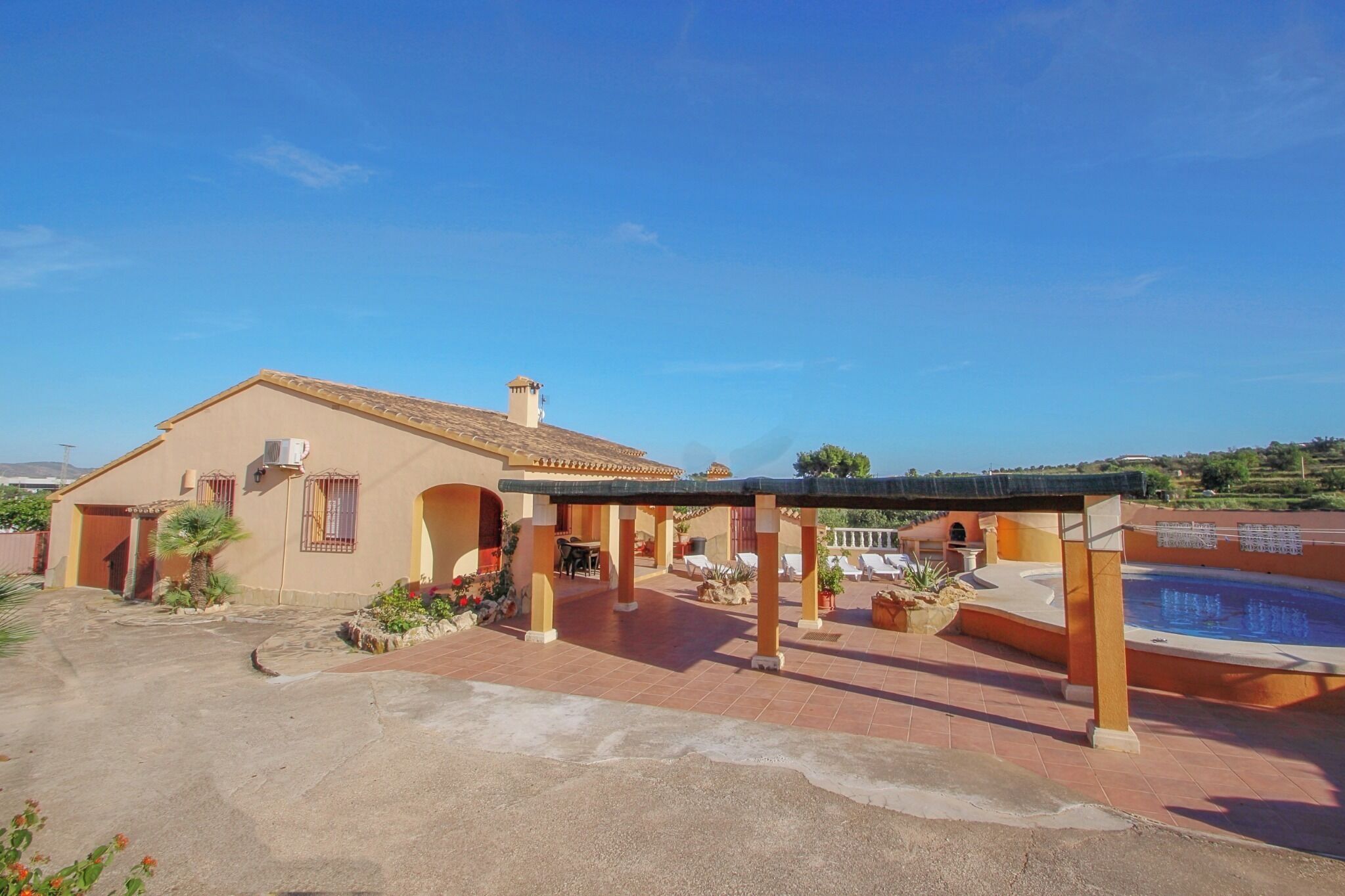 Una casa con porche cubierto, piscina y jardín.