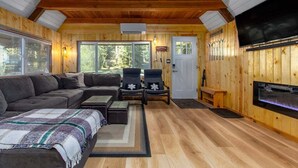 A cozy cabin interior with a large couch, two armchairs, a fireplace, and a TV. - Tee & Ski Cabin | Mt Rainier, White Pass (Packwood)