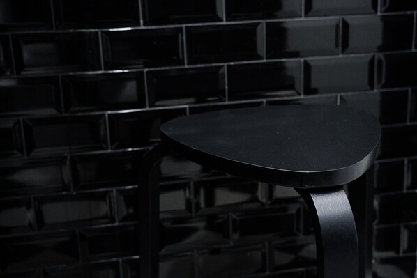 Un tabouret en métal noir, doté d’un pied incurvé, est adossé à un mur carrelé.