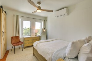 Une chambre à coucher comprenant un lit, un bureau, une chaise, un ventilateur de plafond et une fenêtre.