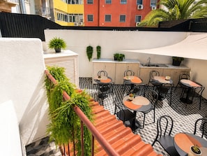 Una terraza en la azotea con mobiliario exterior, una zona de cocina y plantas en macetas.