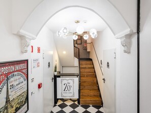 Een gang met een geruit vloerkleed, een trap en een bordje met de tekst 'the 20's rooms & suites'.