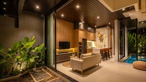 Una sala de estar moderna con un sofá, un televisor y una cocina visible a través de una puerta abierta.