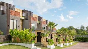 Un moderno edificio residencial de varios pisos con fachada de piedra, grandes ventanales y un jardín bien cuidado con plantas tropicales.