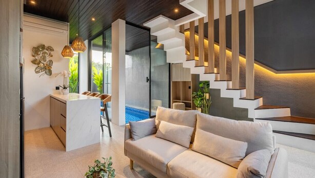 Una sala de estar moderna con un sofá, un comedor con sillas y una escalera con iluminación integrada.