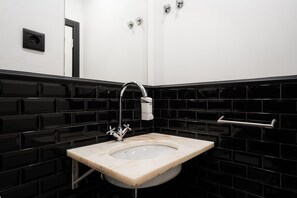 A bathroom with a black tiled wall, a white sink, and a chrome faucet. - The Twenties by GuestReady - Room 11 (Lisbon)