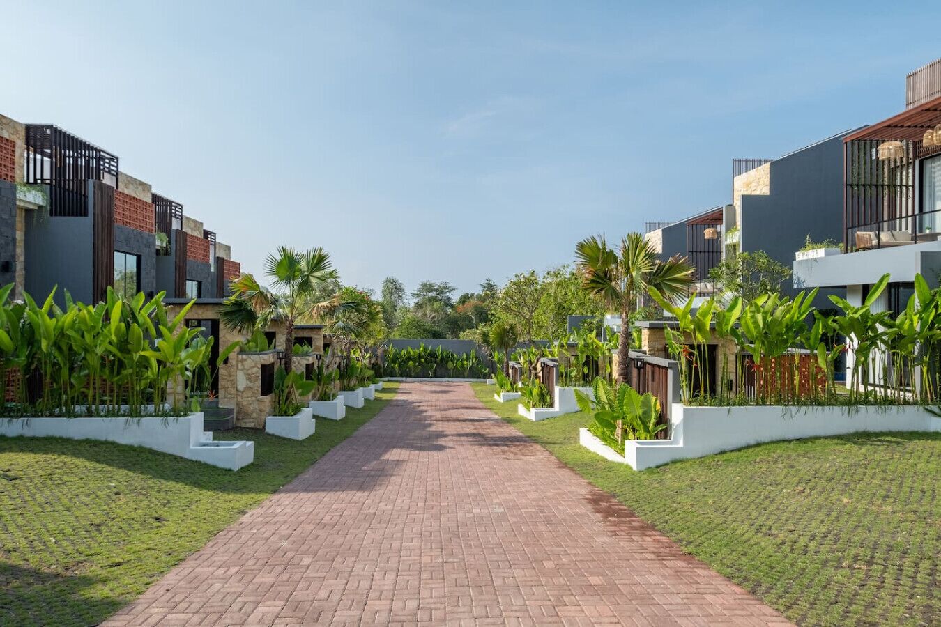 Un vialetto conduce a una fila di edifici moderni con fioriere bianche e vegetazione.