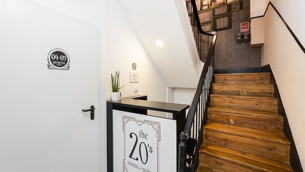 Una escalera con peldaños de madera y barandillas negras, que lleva a un rellano con una puerta blanca identificada con