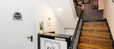 A staircase with wooden steps and black railings, a white door with a sign indicating '04-05 Quartos rooms,' and a sign on the wall advertising 'the 20's rooms & suites.'