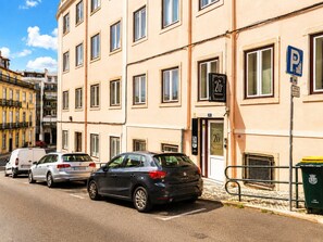 Un immeuble à plusieurs étages, avec un commerce au rez-de-chaussée, un panneau indiquant un parking et une poubelle.