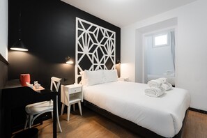 A hotel room with a bed, bedside table, chair, desk, and a decorative wall panel.