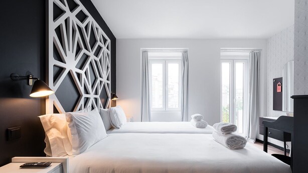 A modern hotel room with two beds, a desk, and a large window.