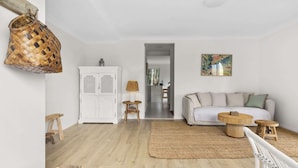 Un salón con un sofá blanco, un tapete tejido y un mueble blanco con puertas decoradas.