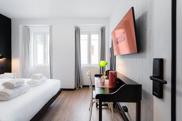 Een hotelkamer met een bed, een bureau met lamp, een koffiezetapparaat en een wandgemonteerde televisie.