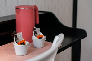Een rode thermosfles en twee witte bekers met koffieportiezakjes op een tafel.