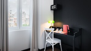 Habitación de hotel con escritorio, silla, lámpara y cafetera.