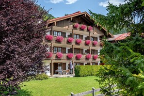A multi-story hotel with balconies adorned with flowers, a well-maintained lawn, and a wooden fence. - Heustub'n Vacation Apartment (Reit im Winkl)