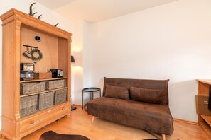 A cozy living room with a brown sofa, a wooden cabinet with baskets, and a small round table. - Heustub'n Vacation Apartment (Reit im Winkl)