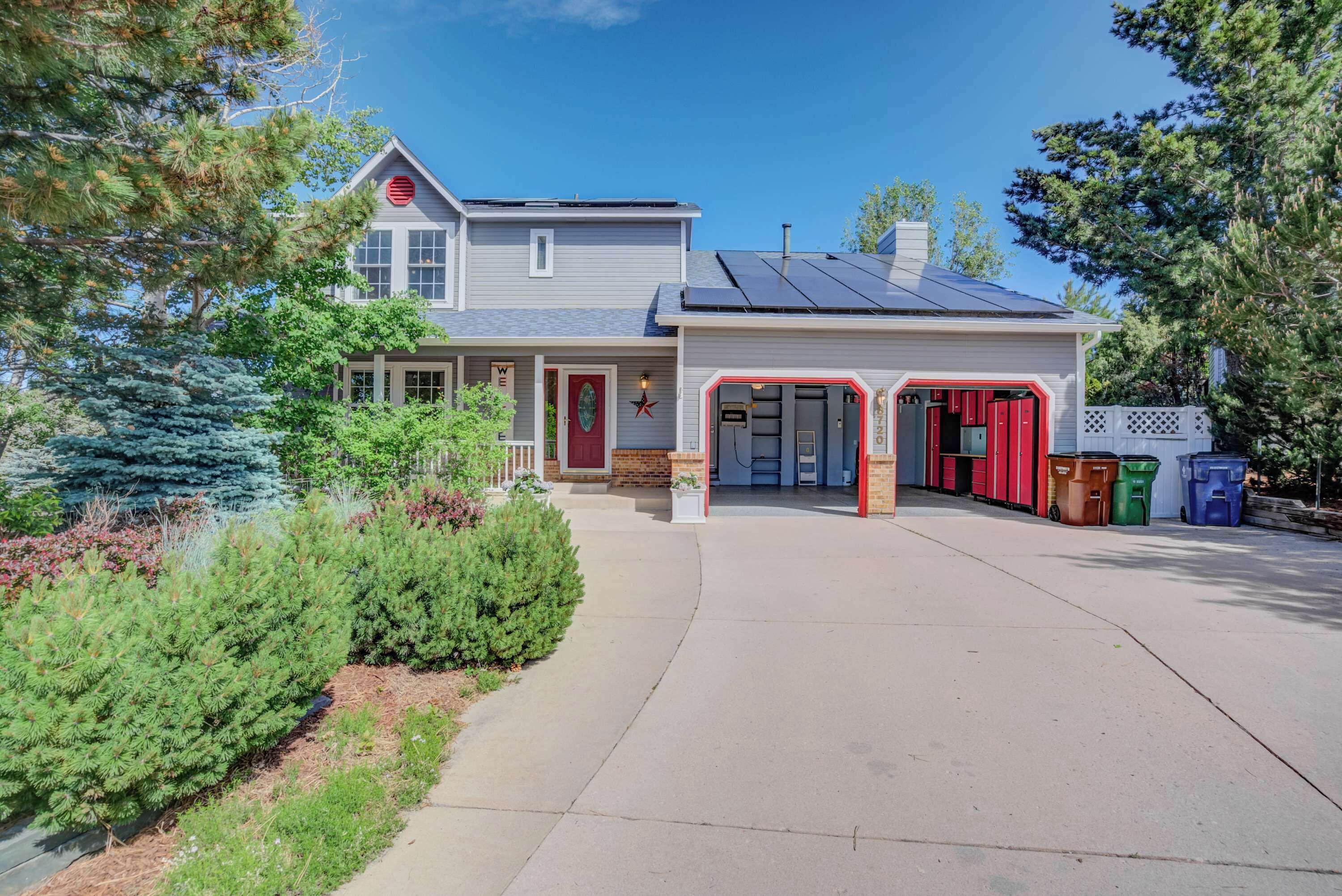 A two-story house with a garage, solar panels, and a front yard with various plants.