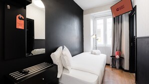 Habitación de hotel con cama, escritorio, espejo, televisor y ventana con cortinas.